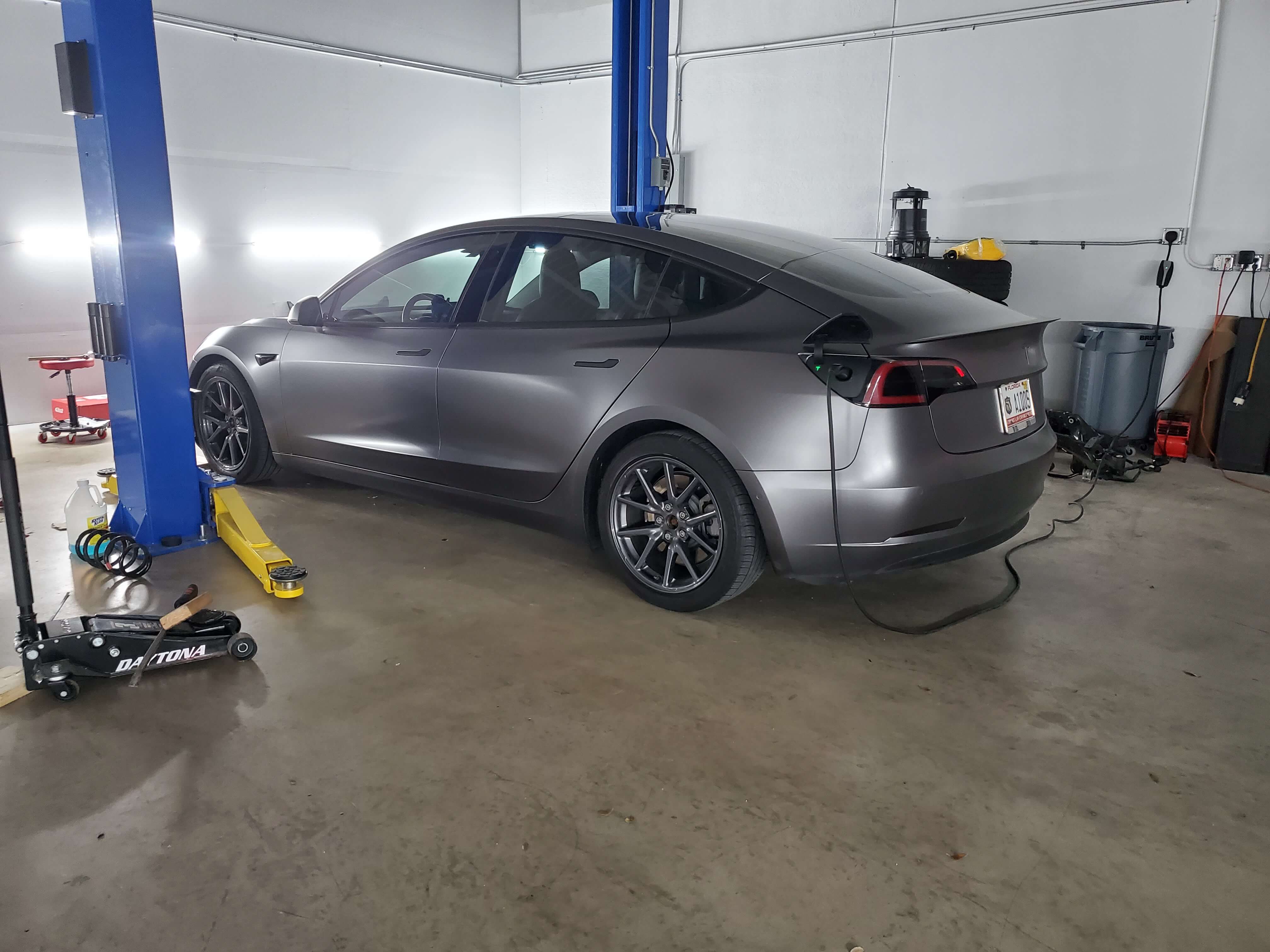 Tesla EV in a service bay with lift, shop tools, and charging equipment visible